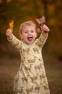 Young girl smiling and holding autumn leaves in a warm golden forest during a playful outdoor fall portrait session in Louisville, Kentucky.