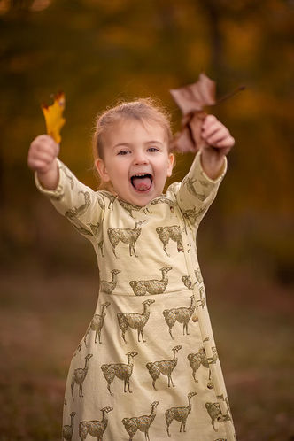 Young girl smiling and holding autumn leaves in a warm golden forest during a playful outdoor fall portrait session in Louisville, Kentucky.
