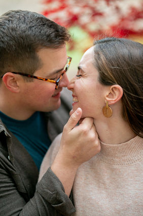 Close-up portrait of a smiling couple touching noses during a candid engagement session in the Highlands neighborhood in Louisville, Kentucky with soft autumn colors in the background.