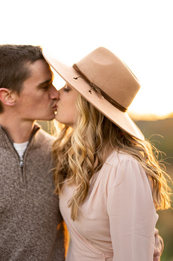 Couple kissing during golden hour engagement session with wide brim hat