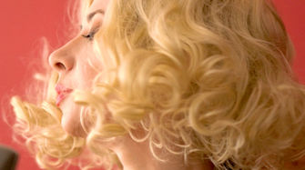 Close up from Emily Carmen’s music video in 1950s glam styling with soft blonde curls, capturing a moment of poised restraint