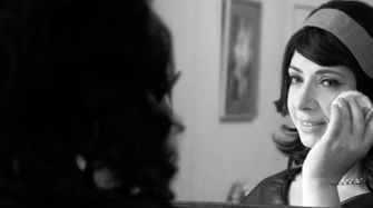 Still from 1950s Housewife Music Video Of Emily Carmen looking in the mirror while usig a powder puff and smiling