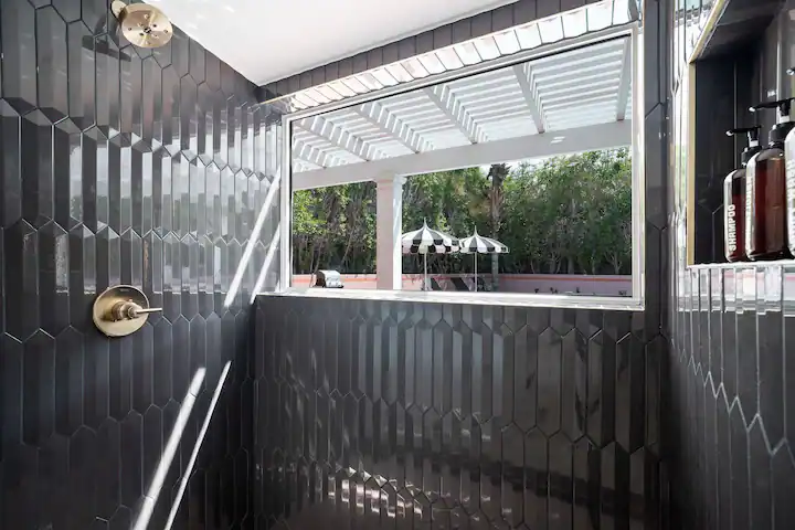 shower in palm desert vacation rental with modern black tile and open window to backyard with private pool