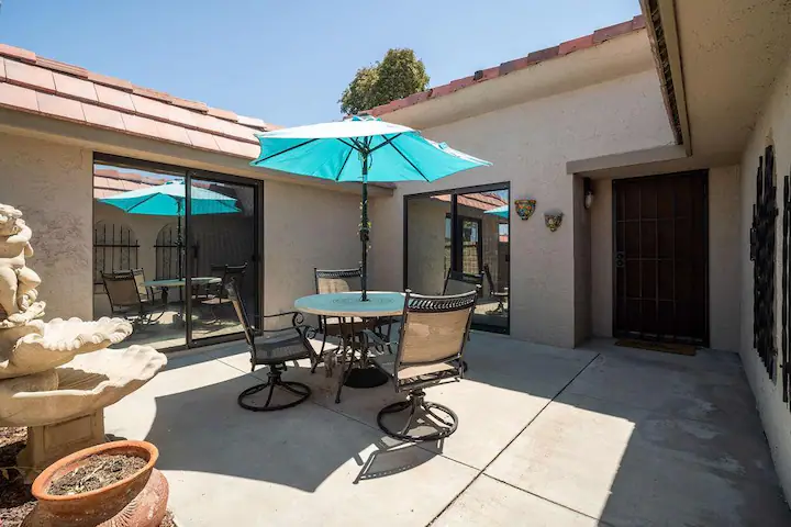 outdoor patio in cathedral city vacation rental with stone fountain and patio table with blue umbrella