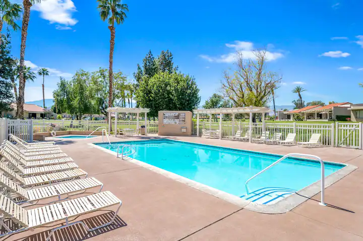 a quiet community pool at a coachella valley vacation rental with lounge chairs and large palm trees