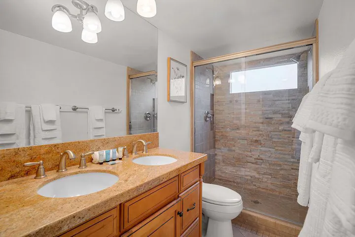 a bathroom in Palm Desert rental property with a double vanity and large shower with natural stone and glass sliding doors