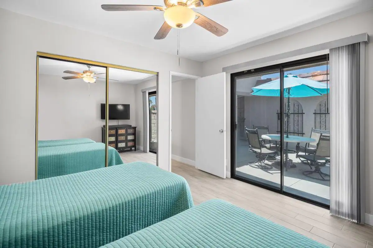 secondary bedroom in Coachella valley rental home with two twin beds, closet with mirrored sliding door, and glass door to outside patio