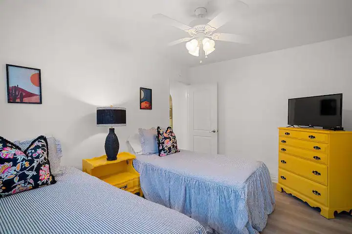 a secondary bedroom with two twin beds, a yellow night stand, and a yellow dresser with television on top
