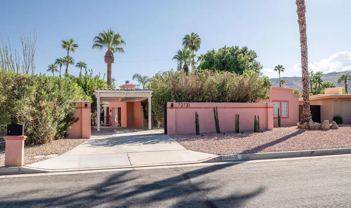 street view of palm desert vacation rental with pink stucco, driveway, and palm trees