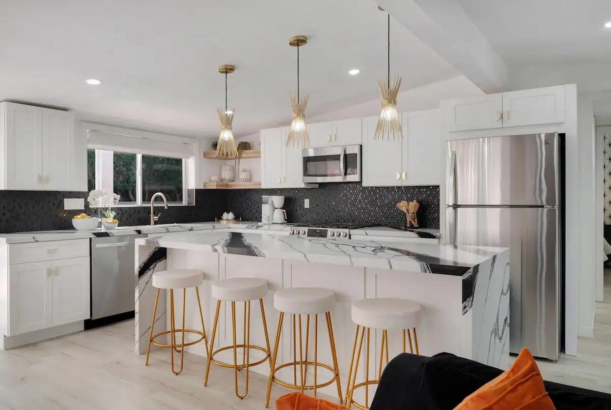 open concept kitchen in modern palm desert vacation rental with marble countertops, black tile backsplash, and stainless steel appliances