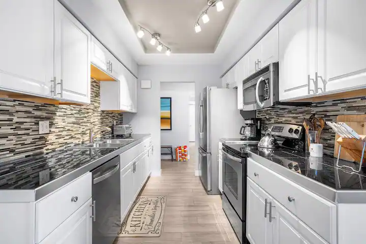 galley kitchen in cathedral city vacation rental with tile backsplash and stainless steel fridge, microwave, dishwasher, and stove