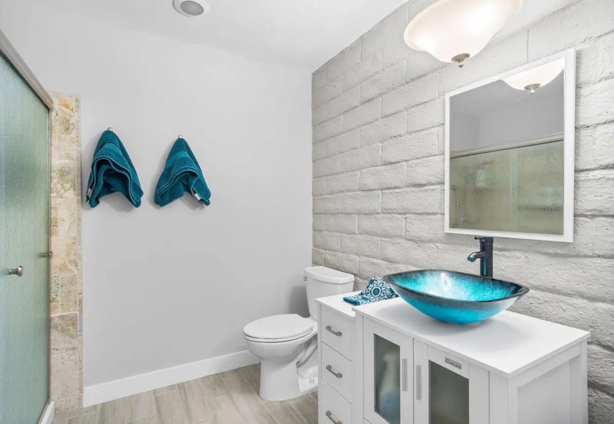 bathroom in cathedral city vacation rental with white brick wall and basin sink with cabinet storage