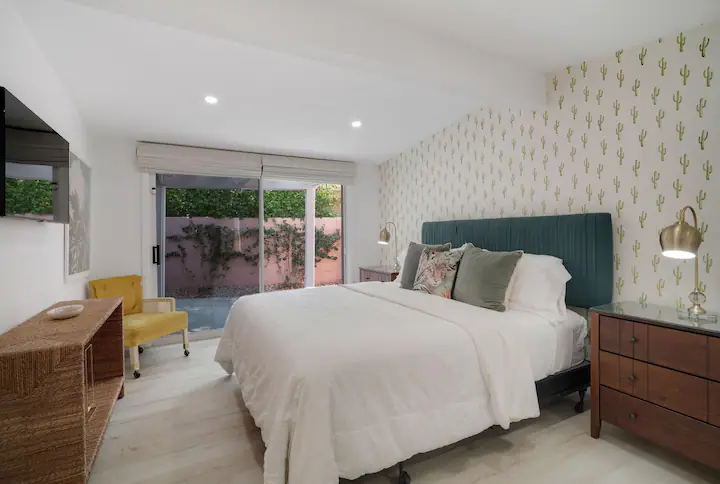 bedroom in palm desert vacation rental with cactus wallpaper accent wall, large velvet bed, and sliding glass door to backyard with private pool
