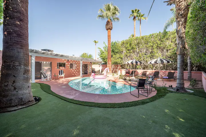 Backyard of palm desert vacation rental with private pool surrounded by green turf, palm trees, and lounge chairs