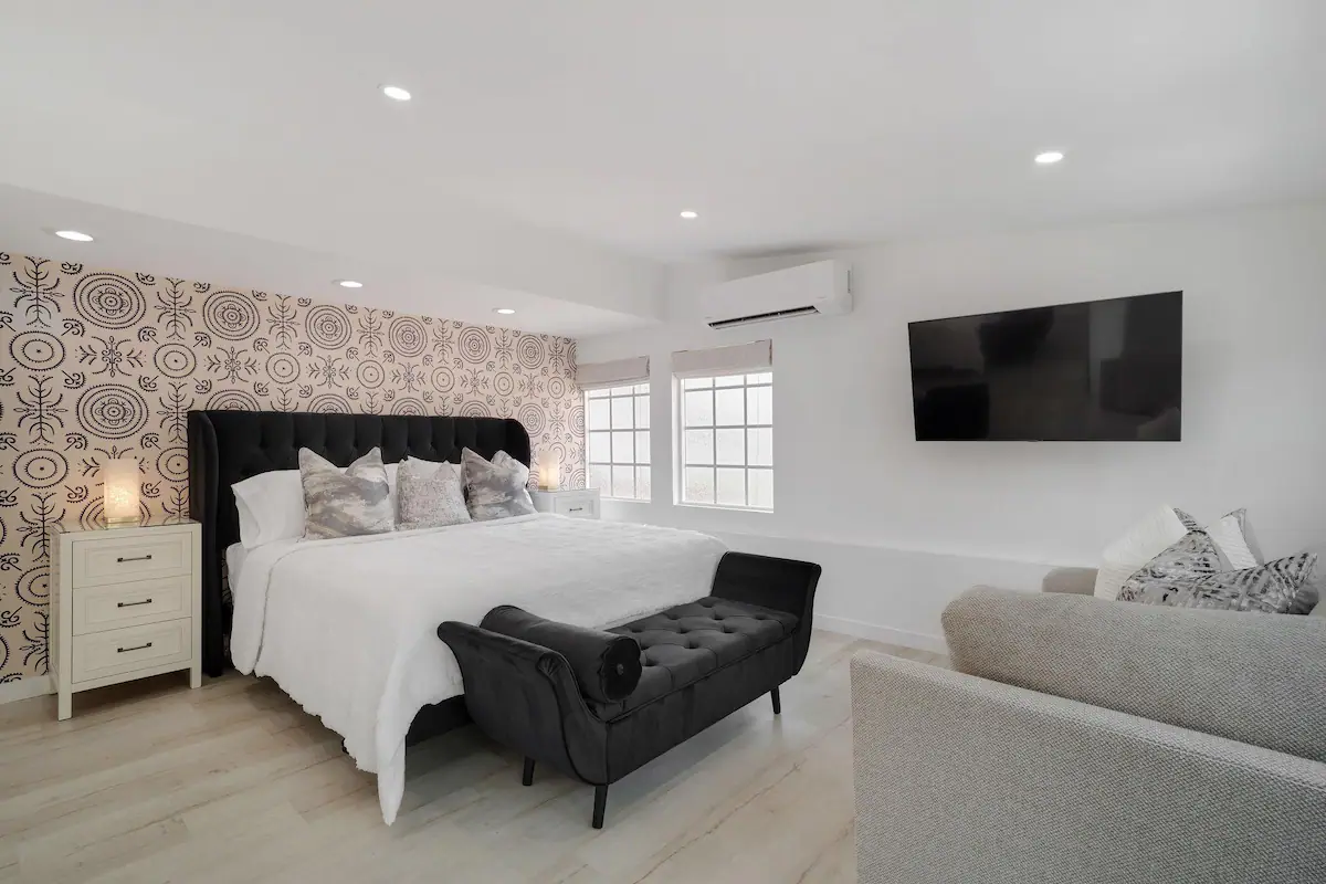 master bedroom in palm desert vacation rental with large velvet bed, wallpapered accent wall, flat screen tv, and couch.