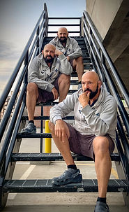 A dynamic, creative self-portrait featuring multiple versions of the artist seated on an industrial stairway.