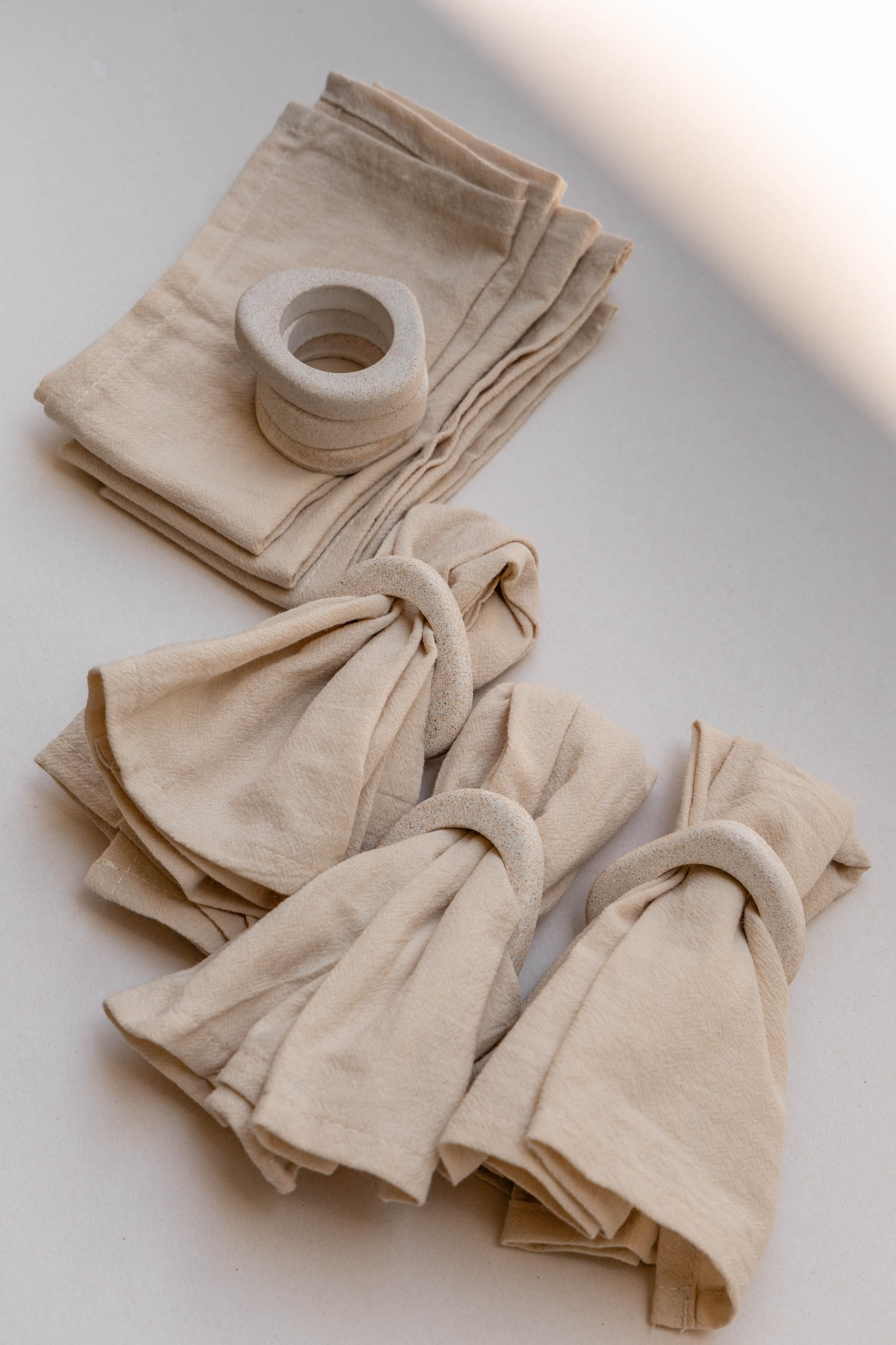 Curated hosting set featuring amorphous sand-textured stone napkin rings and folded natural cotton napkins by VELVART.