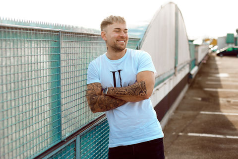 Portrait von Marcel Söhnholz, bekannt aus „Make Love, Fake Love“, aufgenommen bei Sonnenuntergang auf einem Parkplatz. Er trägt ein weißes T-Shirt, ist blond und zeigt sichtbare Tattoos. Professionelles Foto, produziert von SPARKFUL Media.