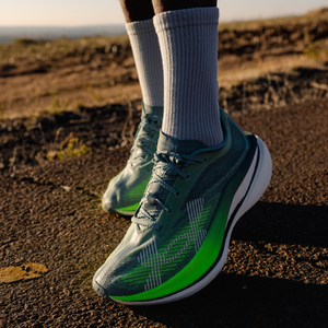 A left side view shot of a runner wearing pair of shoes from the new Under Armour Velociti range on a road with an orange sunset in the background