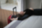 A woman relaxes on a bed next to a red suitcase
