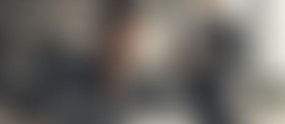 Um homem vestido de blusa cinza clara segurando um documento na mao escrita fgts nao depositado, em um escritorio de advocacia e no fundo uma advogada vestida de blazer cinza e camisa branca esta auxiliando ele em um escritorio com parades cinzas escuras e janelas quadradas.