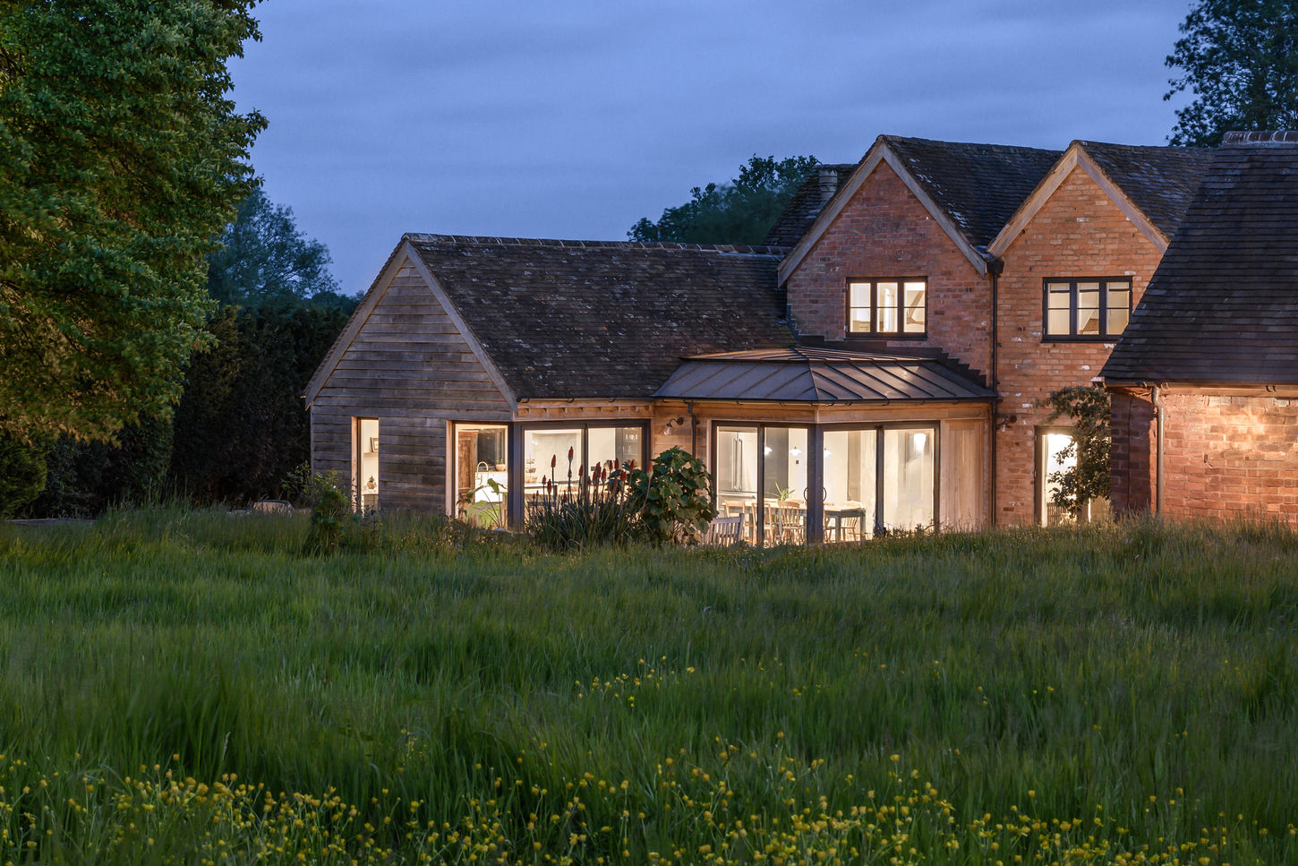 Dusk photograph of a contemporary extension with a copper roof and oak cladding to a Warwickshire farmhouse by design storey