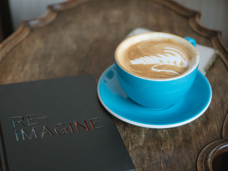 A cup of coffee and a journal that says Re-Imagine