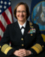 A woman in a Navy officer's dress uniform posing in front of the U.S. and Navy flags