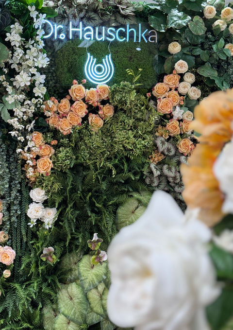 Leuchtendes Dr. Hauschka Logo integriert in eine florale Blumenwand bei einem Markenauftritt