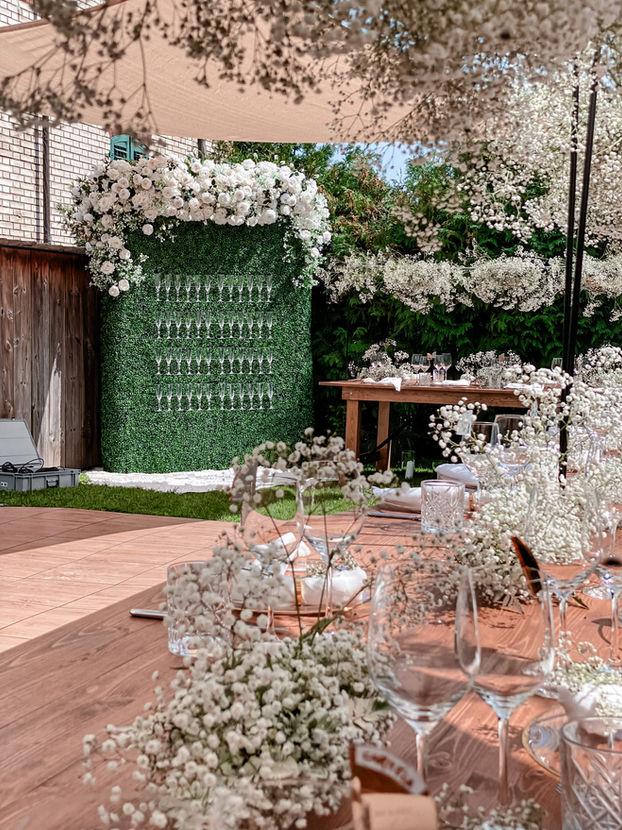 An elegant and romantic summer garden wedding featuring a champagne wall adorned with delicate baby's breath, white roses and hydrangeas. The perfect backdrop for a sophisticated celebration.