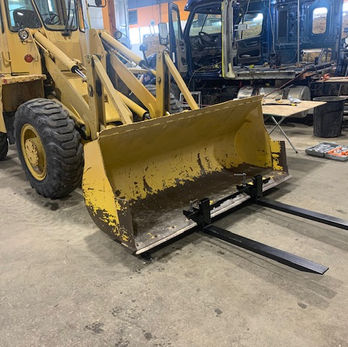 A pair of clamp on bucket forks on a yellow tractor's bucket.