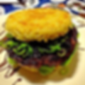 Burger with a crispy ramen noodle bun, dark glazed patty, and green onions on a patterned plate, looking indulgent and quirky