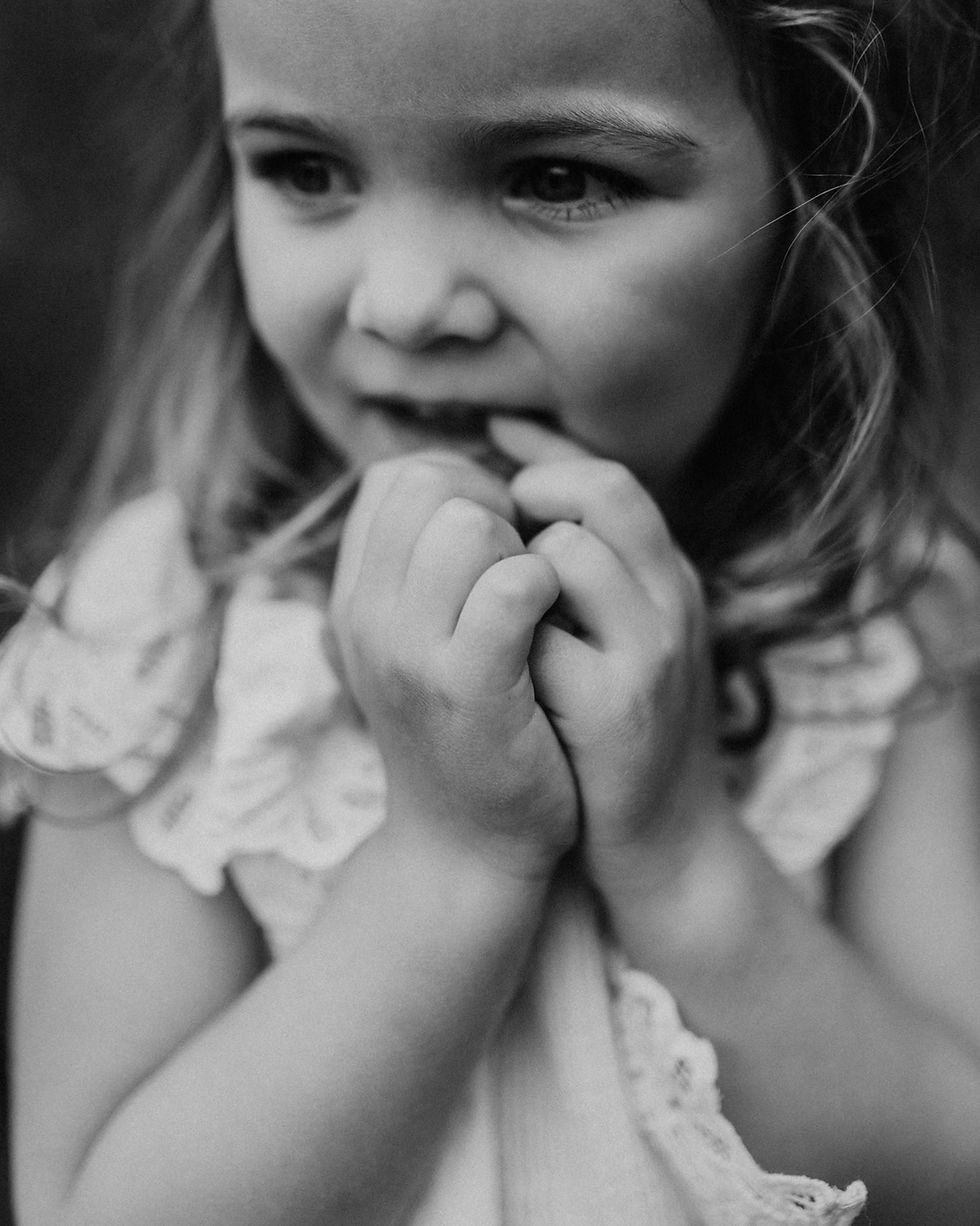 Fillette en gros plan, noir et blanc, se mord les doigts, regard pensif et timide.