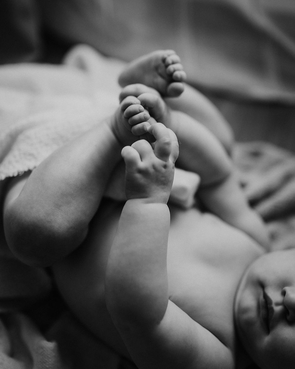 Gros plan en noir et blanc de deux nouveau-nés, leurs petits pieds se touchent sur un lit, ambiance douce et paisible.