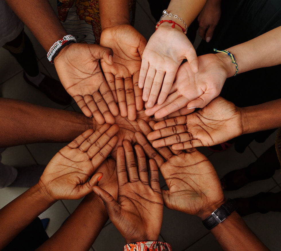 A diverse group of hands forms a circle, palms up, over colorful clothing patterns. The scene evokes unity and diversity against a tiled floor.