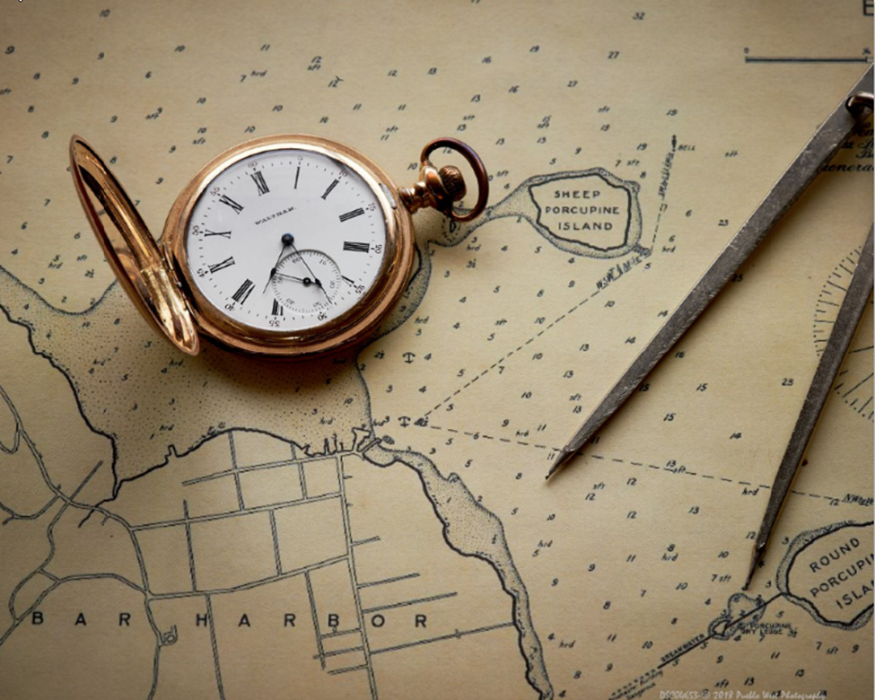 An antique pocket watch rests alongside a pair of navigational dividers on a vintage map, highlighting Sheep Porcupine Island near Bar Harbor.