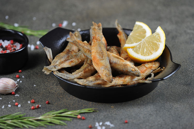Fried smelt fish with lemon slices in a black pan