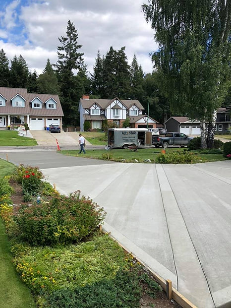A concrete driveway overlooking a suburban neighborhood with a man walking on the road beside a parked truck with a trailer