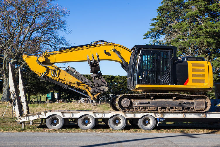 Une grande excavatrice jaune est livrée par camion transporteur sur un chantier