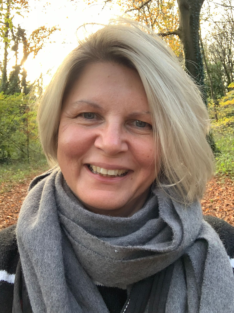 Smiling image of Rachel, the founder, with short blonde hair and gray scarf outdoors.