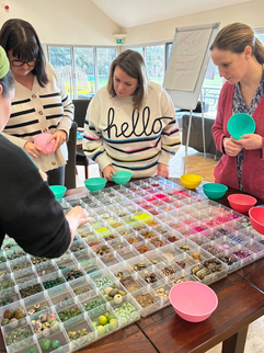 People selecting beads from an organized tray at a party.