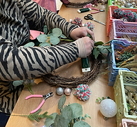 Person crafting a holiday wreath with greenery and baubles