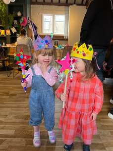 Two young children wearing crowns and holding star wands at a party.