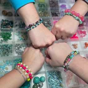 Four people wearing beaded bracelets bump fists above beads.