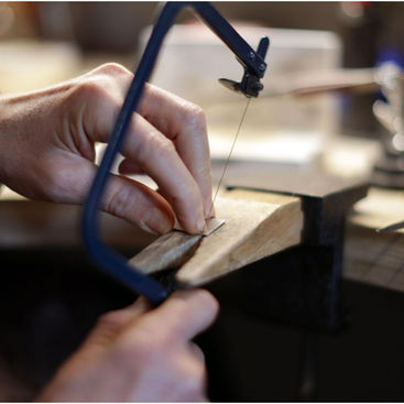 A person carefully sawing metal, focused work on a small wooden work bench