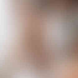 Smiling woman holding food, wearing a necklace. Kitchen in background.