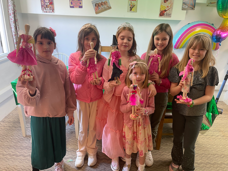Six girls smiling while holding handmade fairy dolls at a party.