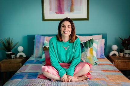 Debbie from Make Space in teal sweater sitting cross-legged on colorful bed in her location home in Chelmsford