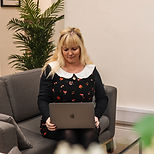 Woman using laptop smiling while sitting on gray couch. Lisa Norfolk Counselling.