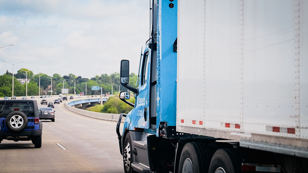 Blue Sagepoint Logistics CNG truck hauling a white trailer on a highway past traffic and an overpass.